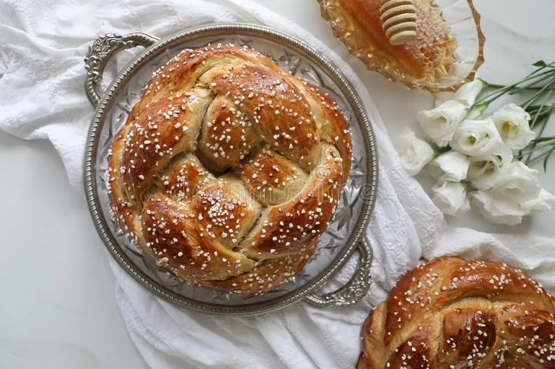Round braided challah topped with pearl sugar on a silver tray, with a honeycomb and white flowers