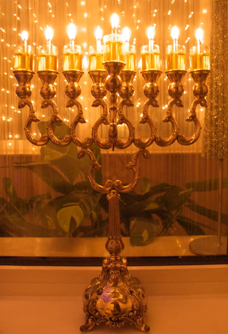 Silver hanukkiah with nine olive-oil lights burning by a window on the last night of Hanukkah