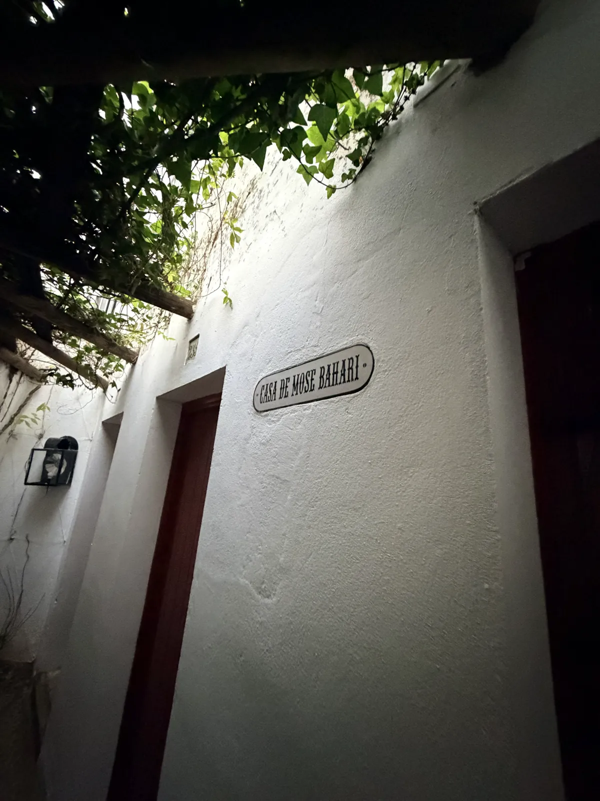 Tafel „Casa de Mose Bahari“ an einer weiß gekalkten Mauer im Barrio de Santa Cruz, neben einer Tür unter einer Weinranke